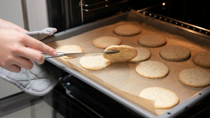 A tray of cookies coming out of the oven. Someone is lifting one cookie to check if the bottom is ready.