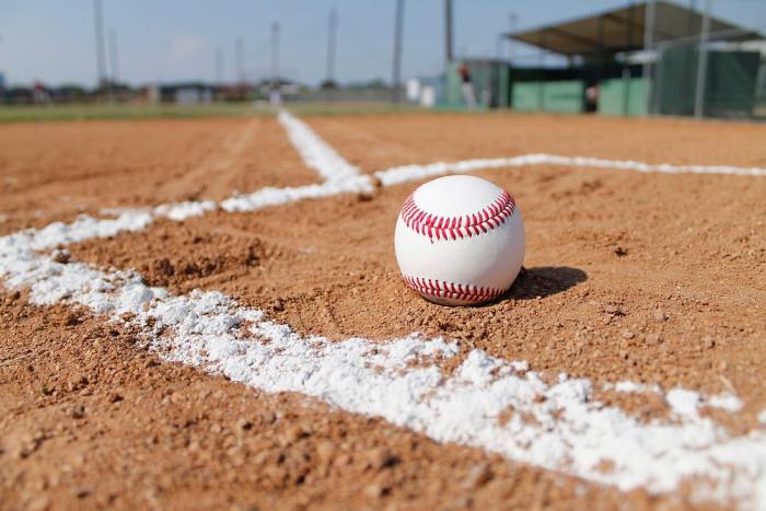 A baseball sitting on the sand of a baseball field inside the lines of the batter's box