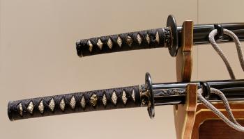 Two samurai swords sitting on a sword rack, showing intricate carvings sit