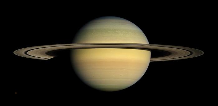 The planet Saturn is shown against the black background of space.  It is bright beige in color, with rings around the center.