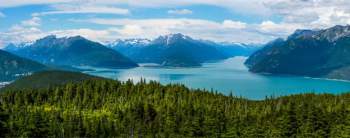 The Alaskan wilderness including hills and mountains, a body of water, and lush forests