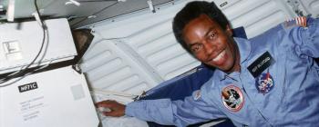 Photo of Guion Bluford in space. He is suspended in zero gravity wearing a blue NASA uniform with a name tag.